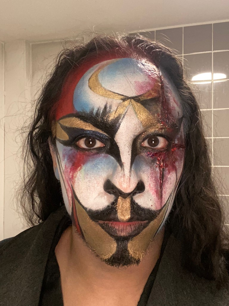 Graphic face paint with gold, colour and a laceration detail